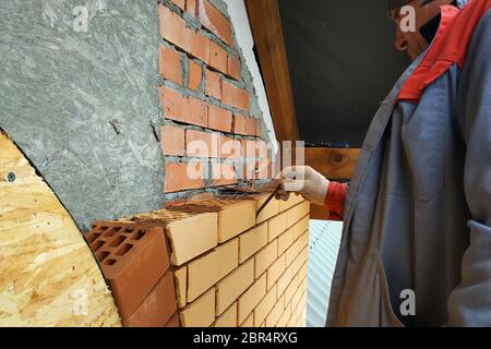 Der Meister in einem blauen Overall baut eine Wand aus Backstein.2020 Stockfoto