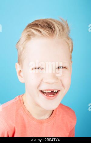 Portrait des niedlichen lachenden Jungen mit stilvoller Frisur in Koralle T-Shirt, Nahaufnahme, auf blauem Hintergrund. Stockfoto