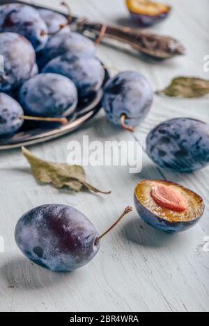 Reife Pflaumen mit in Scheiben geschnittenen Früchte, Blätter und vintage Messer über Licht Holz- Oberfläche Stockfoto