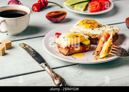 Sandwiches mit Gemüse und Spiegelei auf weissen Teller, Tasse Kaffee und einige Früchte über Holz- Hintergrund. Stockfoto