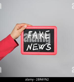Weibliche Hand, die roten Rahmen mit Kreide Inschrift gefälschte Nachrichten auf grauem Hintergrund Stockfoto