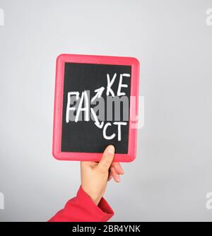 Weibliche Hand, die Kreide Rahmen mit Kreide Inschrift fake und tat, grauer Hintergrund Stockfoto