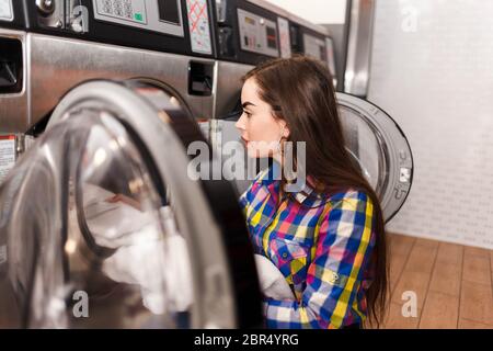 Mädchen lädt Wäsche in eine Waschmaschine. Frau in Waschküche Stockfoto