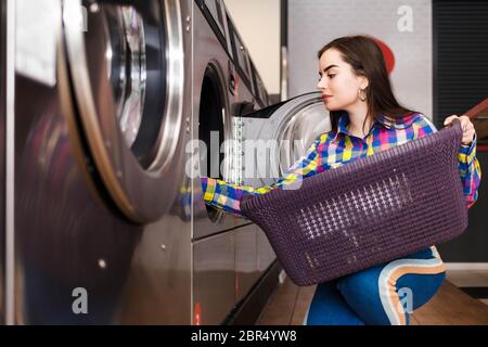 Mädchen lädt Wäsche in eine Waschmaschine. Frau in der öffentlichen Wäscherei Stockfoto