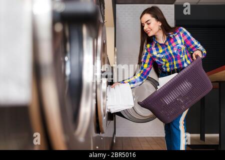 Mädchen lädt Wäsche in eine Waschmaschine. Frau in Waschküche Stockfoto