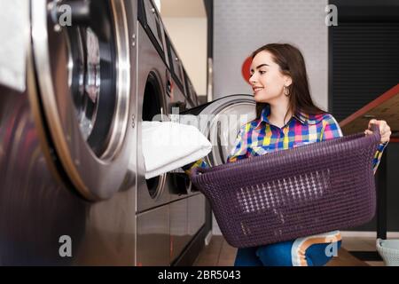 Mädchen lädt Wäsche in eine Waschmaschine. Frau in Waschküche Stockfoto