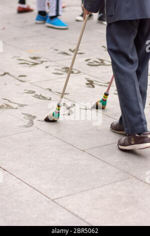 Peking / China - 15. März 2015: Älterer Mann, der in einem Park Wasserkalligraphie (Bodenschrift - dishu) praktiziert. Wasser Kalligraphie ist beliebt Zeitvertreib am Stockfoto