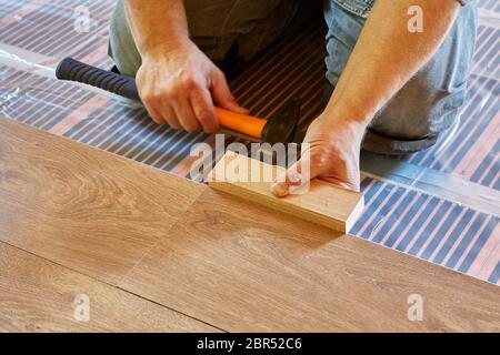 Laminatboden. Der männliche Reparaturmann legt die Platte aus Laminatboden auf einen wärmegedämmten Boden. Elektrische Fußbodenheizung, Heizstrahler, inf Stockfoto