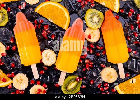 Obst Eis auf Stick mit Scheiben Früchte auf schwarzem Schiefer. Fokus auf Eis am Stiel. Stockfoto