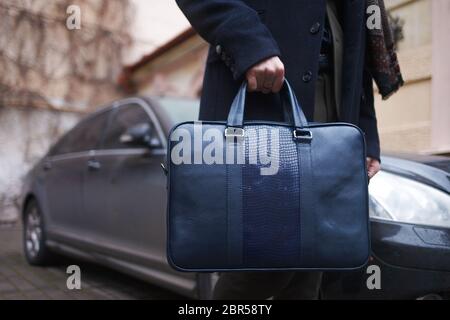 Stilvoll gekleideter Geschäftsmann mit einer Tasche in den Händen steht auf dem Hintergrund seines Autos Stockfoto