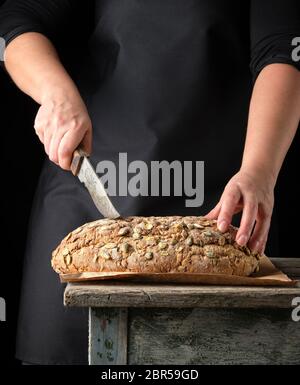 Weibliche Hände halten, ovale, gebackenem Roggenbrot mit Kürbissamen, dunklen Hintergrund Stockfoto