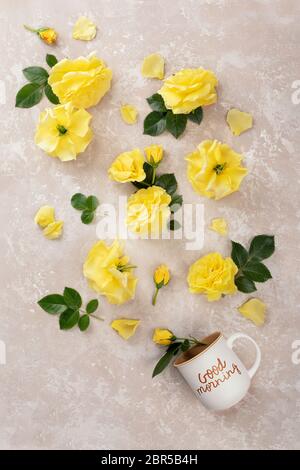 Kreatives Layout aus Tasse Kaffee mit der Aufschrift Guten Morgen und gelben Rosen und Blättern auf rosa Hintergrund. Draufsicht, flaches Lay. Stockfoto