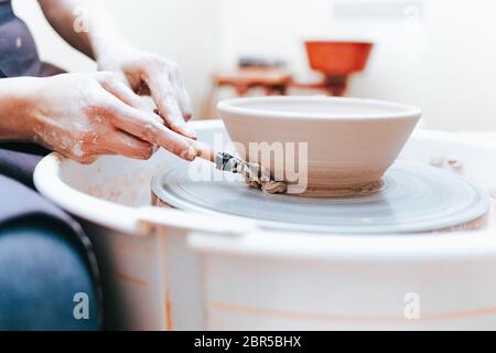 Prozess der Schaffung und Bildung einer weißen Tonkeramikplatte. Professionelle Töpfer ist in der Modellierung Tonplatten beschäftigt. Potter arbeitet in einer Werkstatt Stockfoto