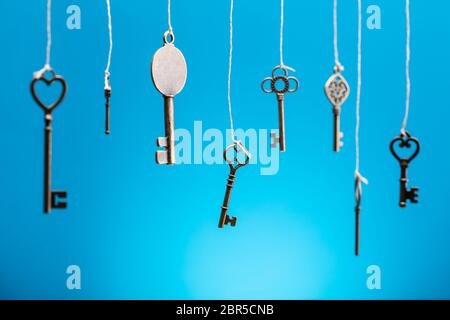 Die alten Schlüssel hängen mit Strings in einer Reihe vor blauem Hintergrund Stockfoto