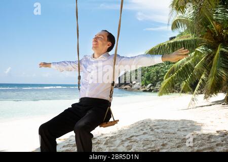 Lächelnden jungen Mann sitzt auf Swing Outstretching seine Hand geniessen die frische Luft am Strand Stockfoto