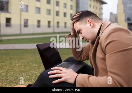 Mann sitzt mit einem Laptop und depressiv wegen der Arbeit. Nachdenklicher Student hält den Kopf Stockfoto