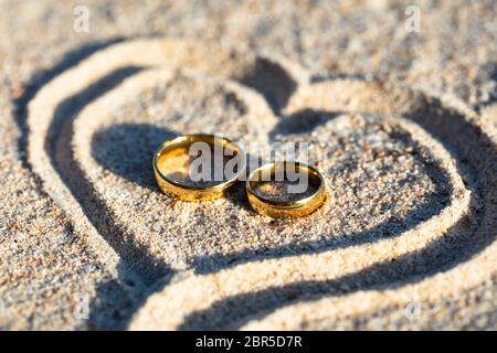 Einen Überblick über die Goldene Hochzeit Ringe Im Herzen Form auf Sand am Strand Stockfoto
