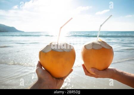 In der Nähe von Paar Hand Kokosnuss mit Trinkhalm Vor der idyllischen Meer Stockfoto