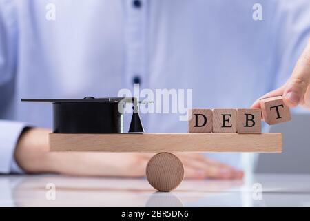 Der Unternehmer Hand Wort Schuld auf Holz- Wippe zum Ausgleich Schwarze Graduierung Hat Stockfoto