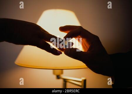 Der Mann legt einen Ring an den Finger seiner Frau gegen eine Lampe. Paar tauschende Ringe aus der Nähe Stockfoto