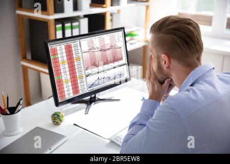 Verzweifelten Geschäftsmann mit finanziellen Verlusten an seinem Schreibtisch consulting Graphen sitzen auf Monitoren konfrontiert Stockfoto