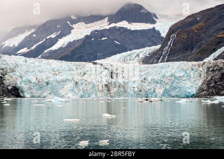 Der Überraschungsgletscher mit der mittleren Moräne und dem in Harriman Fjord in der Nähe von Whittier, Alaska schwimmenden Braseis. Surprise Glacier ist der aktivste kalbende Tauch-Gletscher im Prince William Sound. Stockfoto