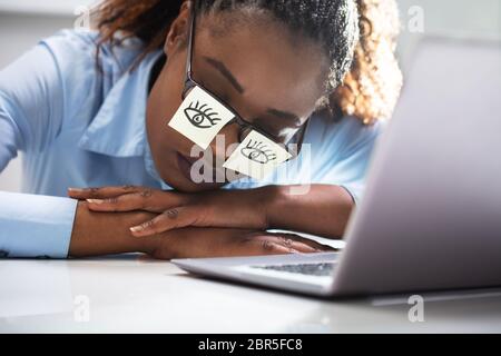 Junge Frau, die Ihre Augen mit Haftnotizen auf dem Schreibtisch im Büro Stockfoto
