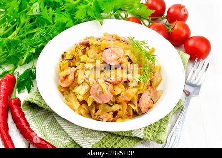 Kohleintopf mit Wurst in eine weiße Platte auf einem Küchenpapier, Tomaten, Petersilie und eine Gabel vor dem Hintergrund der hellen Holzmöbeln board Stockfoto