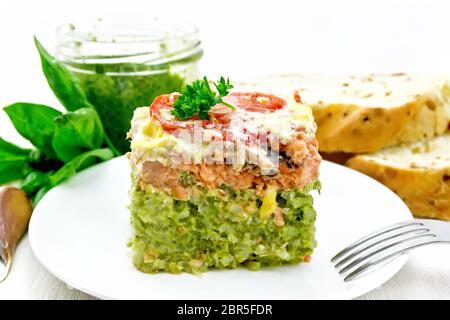 Auflauf mit Lachs und Reis mit Pesto, Tomaten und Käse in der Platte, Brot und ein Glas mit der Soße auf Holzbrett Hintergrund Stockfoto