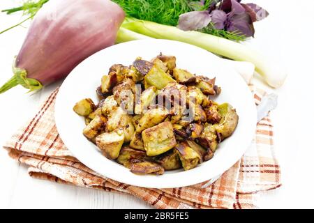 Gebratenen Auberginen mit Zwiebeln, Ei und Gewürze in einer Platte auf eine Serviette, Basilikum, Lauch und Dill auf weißem Holzbrett Hintergrund Stockfoto