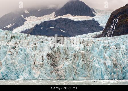 Der Überraschungsgletscher mit der mittleren Moräne und dem in Harriman Fjord in der Nähe von Whittier, Alaska schwimmenden Braseis. Surprise Glacier ist der aktivste kalbende Tauch-Gletscher im Prince William Sound. Stockfoto