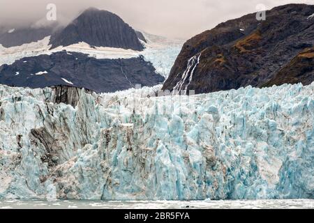 Der Überraschungsgletscher mit der mittleren Moräne und dem in Harriman Fjord in der Nähe von Whittier, Alaska schwimmenden Braseis. Surprise Glacier ist der aktivste kalbende Tauch-Gletscher im Prince William Sound. Stockfoto