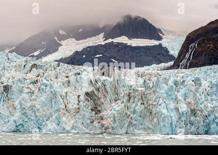 Der Überraschungsgletscher mit der mittleren Moräne und dem in Harriman Fjord in der Nähe von Whittier, Alaska schwimmenden Braseis. Surprise Glacier ist der aktivste kalbende Tauch-Gletscher im Prince William Sound. Stockfoto