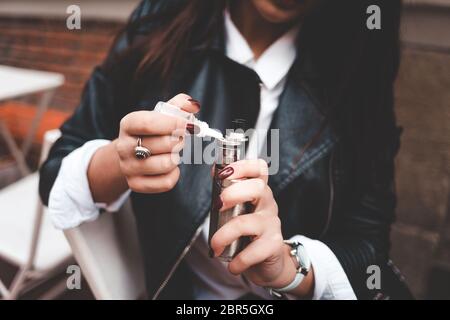 Frau füllt Flüssigkeit in E-Zigarette Nahaufnahme. Mädchen füllt Flüssigkeit in vape. Elektronisches Zigarettenkonzept Stockfoto