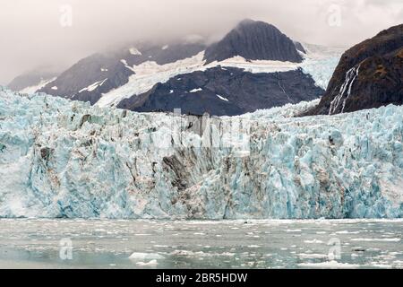 Der Überraschungsgletscher mit der mittleren Moräne und dem in Surprise Inlet, Harriman Fjord, nahe Whittier, Alaska schwimmenden Braseis. Surprise Glacier ist der aktivste kalbende Tauch-Gletscher im Prince William Sound. Stockfoto