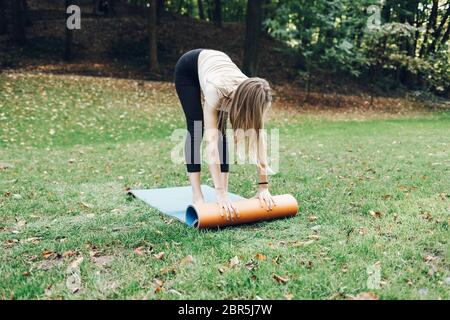 Junge schlanke Mädchen faltet ihren Teppich nach Yoga-Übung Stockfoto