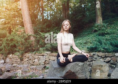 Yoga-Frau sitzt auf einem Stein in Lotusposition. Yoga-Konzept Stockfoto