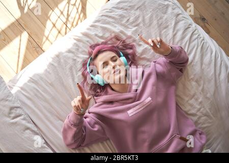 Glückliche Teenager Mädchen rosa Haare tragen Kopfhörer im Bett liegen Musik singen hören. Stockfoto