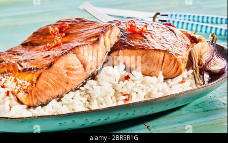 Gourmet Grill oder Ofen pikante Lachssteaks mit roter Chili auf einem Bett aus Reis mit gerösteten Zwiebeln in der Nähe zu sehen, die Werbung für ein Menü serviert. Stockfoto