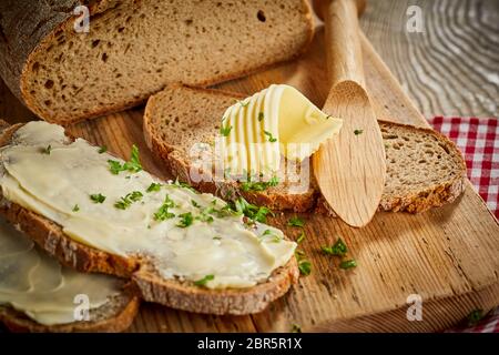 Gebutterte Scheiben frisches Roggenbrot mit gehackter Petersilie und eine dekorative Note ergänzt oder curl von Butter auf einem Holzbrett mit Spreuverteiler oder Butter knif Stockfoto