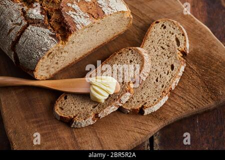 Scheiben und Laib frisches knuspriges Bauernbrot auf einem Holzbrett mit Spreuverteiler oder Butter Messer und klacks Butter in einem hohen Winkel anzeigen Stockfoto