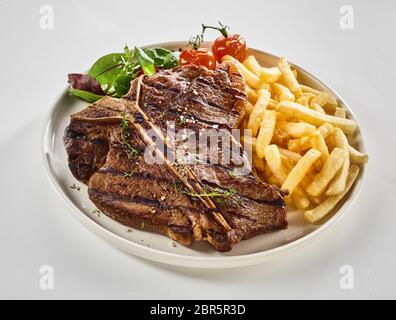 Gegrillte T-Bone Steak mit Pommes frites und frischem grünen de gewürzt mit Kräutern und auf einem Teller serviert über Weiß für Menü Werbung Stockfoto