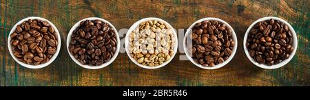 Panorama Banner mit verschiedenen frisch gerösteten und rohe Kaffeebohnen in den einzelnen Schalen auf rustikalem Holz von oben nach unten gesehen Stockfoto