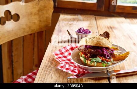 Leckere Spezialität wild wild Beef Burger auf ein knuspriges Brötchen mit Kartoffelecken serviert auf einem rustikalen Tisch mit roten und weißen überprüft Serviette in einer Taverne oder Stockfoto