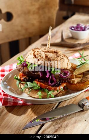 Spezialität wild wild Burger auf ein knuspriges Brötchen mit frischem Salat Zutaten getrimmt und serviert mit Kartoffelecken in einer Nahaufnahme, Seite, Ansicht auf einem rustikalen Stockfoto