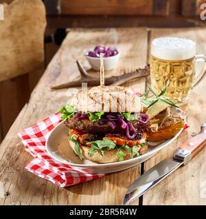 Wild Wild Burger mit frischem Salat Beilagen auf einem crusty Roll serviert für eine Taverne Mittagessen mit humpen kaltes Bier auf eine Tabelle mit Rehen ant eingerichtet Stockfoto