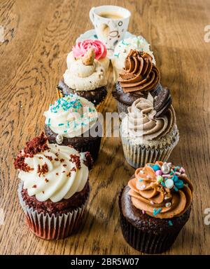 Kleine Cupcakes mit einer Vielzahl von Sahne auf einem Eichentisch und schwarzem Kaffee in einer Tasse aufgereiht Stockfoto