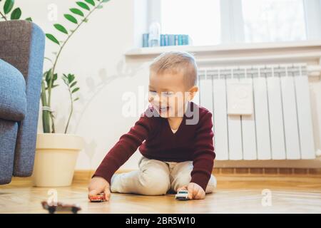 Schöner Junge spielt auf dem Boden mit einigen Spielzeugautos und lacht fröhlich Stockfoto