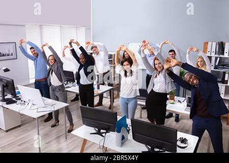 Gruppe von lächelnden multi-ethnischen Geschäftsleute tun Stretching Übung am Arbeitsplatz Stockfoto