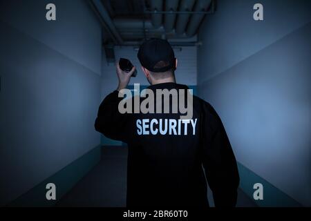 Rückansicht eines männlichen Wachmann mit Taschenlampe stehend im Flur Stockfoto